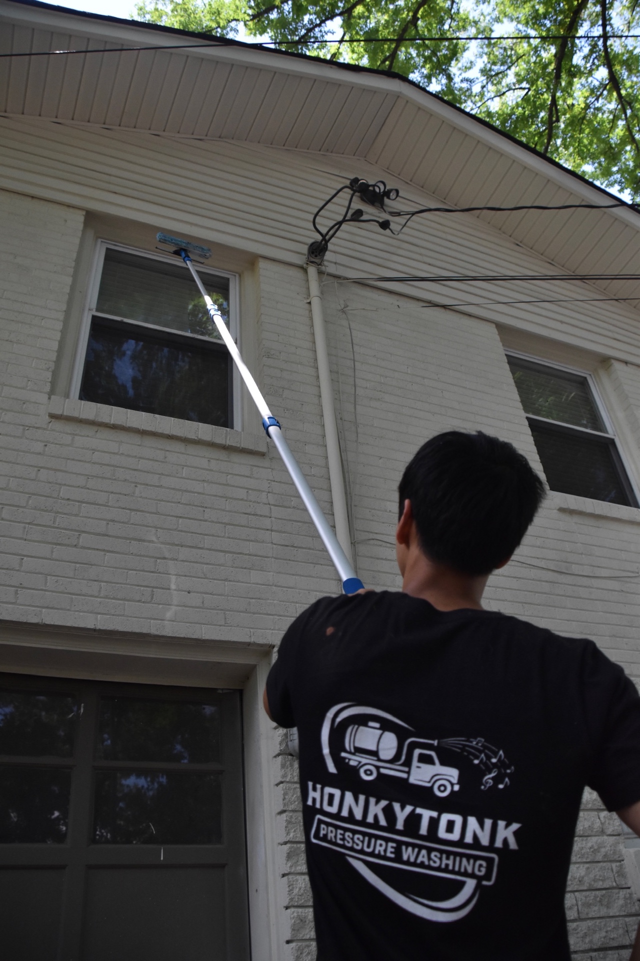 Honky Tonk Pressure Washing cleaning second-story windows with a water-fed extension pole on a white brick home in Nashville, TN